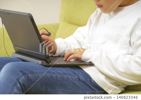 A child studying on a computer while sitting on the sofa. A child studying on a computer while sitting on the sofa. 140823348