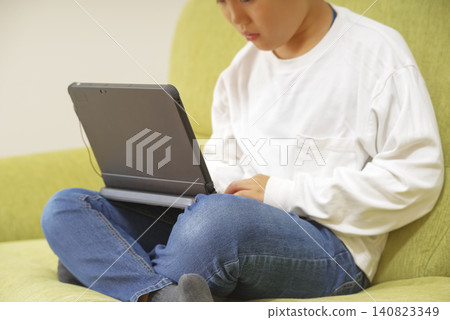 A child studying on a computer while sitting on the sofa. A child studying on a computer while sitting on the sofa. 140823349