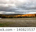 A dramatic autumn landscape of mountains adorned with autumn foliage, illuminated by the setting sun, against a stunning autumn sky. 140823537