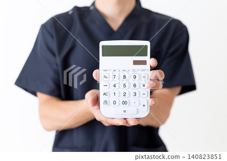 A middle-aged male doctor wearing navy blue scrubs and holding a white calculator. A middle-aged male doctor wearing navy blue scrubs and holding a white calculator. 140823851