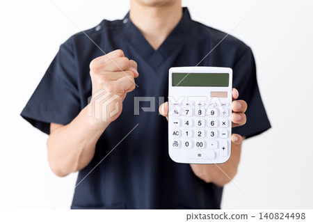 A middle-aged male doctor in navy blue scrubs makes a triumphant gesture while holding a white calculator. A middle-aged male doctor in navy blue scrubs makes a triumphant gesture while holding a white calculator. 140824498