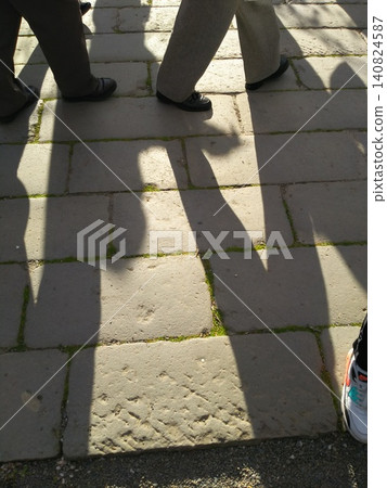 The shadows of people's feet are cast on the cobblestones as they pass by. The shadows of people's feet are cast on the cobblestones as they pass by. 140824587