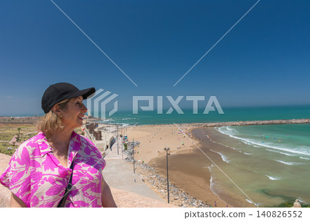 A mature tourist smiles as she gazes at the beach in Rabat and the Bouregreg River from the Kasbah of the Udayas. A mature tourist smiles as she gazes at the beach in Rabat and the Bouregreg River from the Kasbah of the Udayas. 140826552