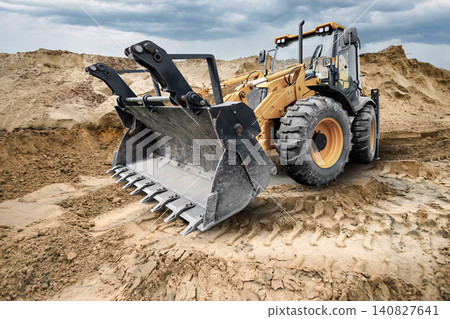 A universal excavator loader is at a construction site moving dirt and preparing the area for upcoming work. The scene shows heavy equipment in operation A universal excavator loader is at a construction site moving dirt and preparing the area for upcoming work. The scene shows heavy equipment in operation 140827641