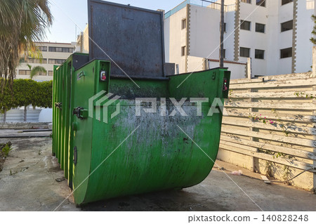 Industrial green waste compactor dumpster with an open lid in an urban service area, symbolizing waste management, recycling, sanitation, and environmental responsibility Industrial green waste compactor dumpster with an open lid in an urban service area, symbolizing waste management, recycling, sanitation, and environmental responsibility 140828248