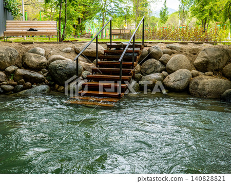 Wooden stairs descending into natural river with rocky shore and green trees, nature recreation and outdoor travel concept Wooden stairs descending into natural river with rocky shore and green trees, nature recreation and outdoor travel concept 140828821