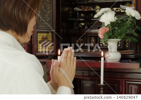 A woman prays with her hands clasped together in front of a Buddhist altar. A woman prays with her hands clasped together in front of a Buddhist altar. 140829047