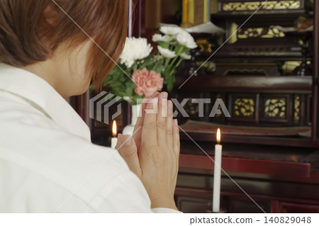 A woman prays with her hands clasped together in front of a Buddhist altar. A woman prays with her hands clasped together in front of a Buddhist altar. 140829048