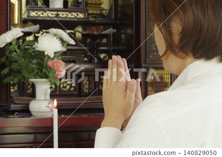 A woman prays with her hands clasped together in front of a Buddhist altar. A woman prays with her hands clasped together in front of a Buddhist altar. 140829050