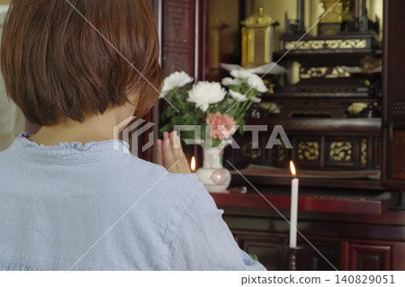 A woman prays with her hands clasped together in front of a Buddhist altar. A woman prays with her hands clasped together in front of a Buddhist altar. 140829051