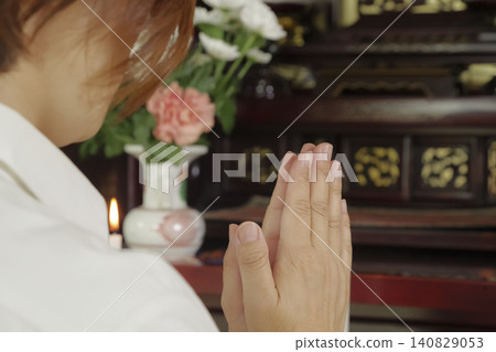 A woman prays with her hands clasped together in front of a Buddhist altar. A woman prays with her hands clasped together in front of a Buddhist altar. 140829053