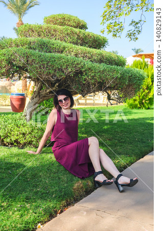 A woman sits playfully on the grass under the canopy of a tree 140829143