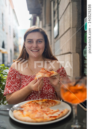 Happy young woman eating delicious Italian pizza at outdoor cafe in Europe 140829286