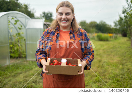 Happy young woman farmer holding strawberry box in garden Happy young woman farmer holding strawberry box in garden 140830796