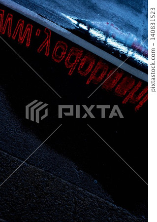 On a rainy night street, the abstract reflection of red neon letters shimmers in puddles. On a rainy night street, the abstract reflection of red neon letters shimmers in puddles. 140831523