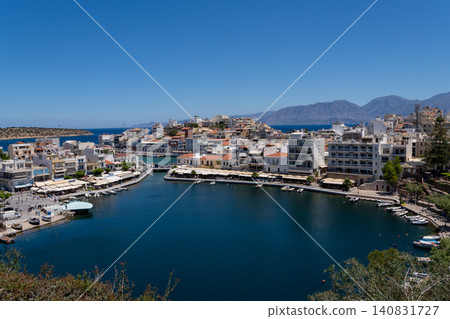 Elevated panoramic view of Lake Voulismeni port and Agios Nikolaos coastal resort city under blue sky, Crete, Greece Elevated panoramic view of Lake Voulismeni port and Agios Nikolaos coastal resort city under blue sky, Crete, Greece 140831727