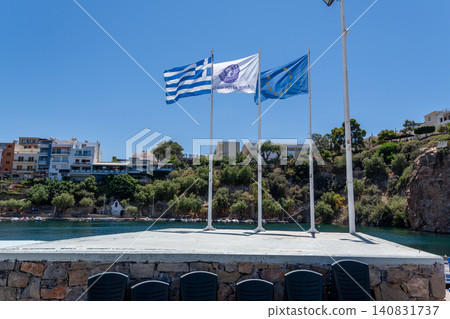 National flag of Greece European Union flag and Agios Nikolaos municipality flag on masts at Lake Voulismeni port, Crete, Greece National flag of Greece European Union flag and Agios Nikolaos municipality flag on masts at Lake Voulismeni port, Crete, Greece 140831737