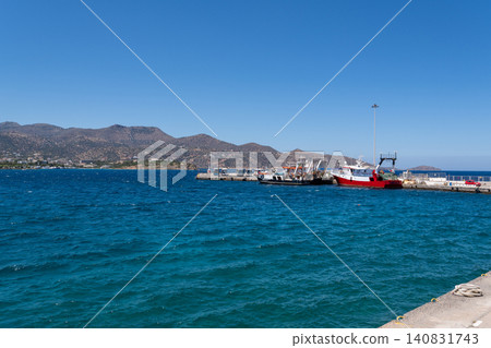 Fishing boats and ships docked at the concrete pier of Agios Nikolaos port under clear blue sky, Crete, Greece 140831743