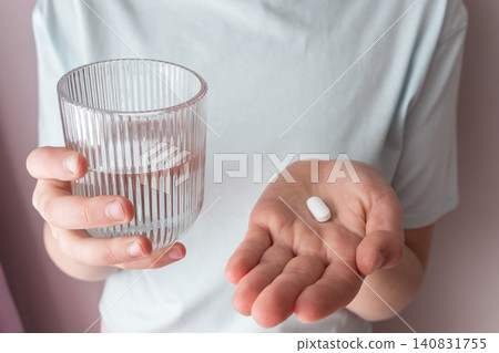 Girl in white clothes take the pill and glass with water in the hand. Healthcare from pharmacy. Kid sit at home because of illness. Girl in white clothes take the pill and glass with water in the hand. Healthcare from pharmacy. Kid sit at home because of illness. 140831755