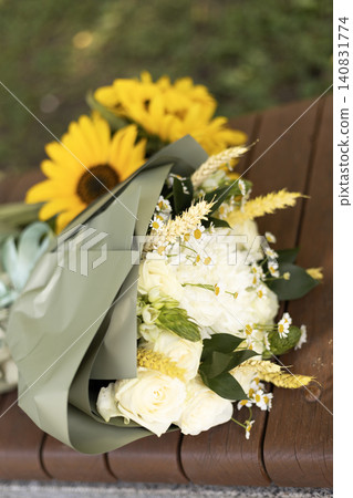Sunflower and white rose bouquet wrapped in green paper on a wooden bench Sunflower and white rose bouquet wrapped in green paper on a wooden bench 140831774