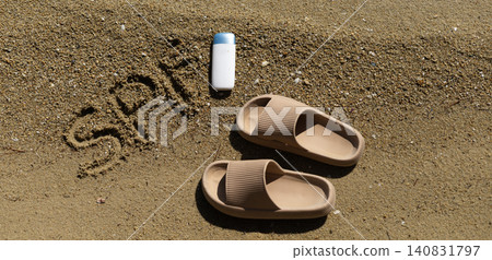 Sunscreen bottle, sandals and SPA inscription on textured beach sand 140831797
