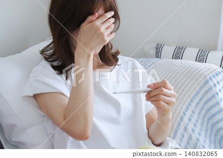 一位覺得身體不適的女士用體溫計測量體溫。 一位覺得身體不適的女士用體溫計測量體溫。 140832065