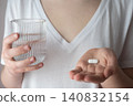 Girl in white clothes take the pill and glass with water in the hand. Healthcare from pharmacy. Kid sit at home because of illness. 140832154