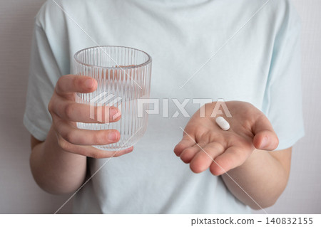 Girl in blue t-shirt take the pill and glass with water in the hand. Healthcare from pharmacy. Kid sit at home because of illness. Girl in blue t-shirt take the pill and glass with water in the hand. Healthcare from pharmacy. Kid sit at home because of illness. 140832155