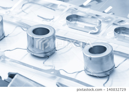 A high-precision metal deep drawing sample part on a strip material in a blue tone scene. A high-precision metal deep drawing sample part on a strip material in a blue tone scene. 140832729