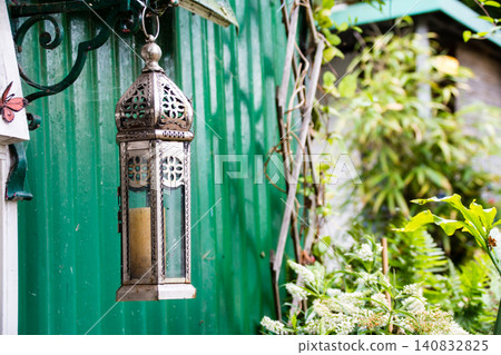 A retro lamp hanging on a wall surrounded by greenery, on Eel Pie Island, a suburb of London. A retro lamp hanging on a wall surrounded by greenery, on Eel Pie Island, a suburb of London. 140832825