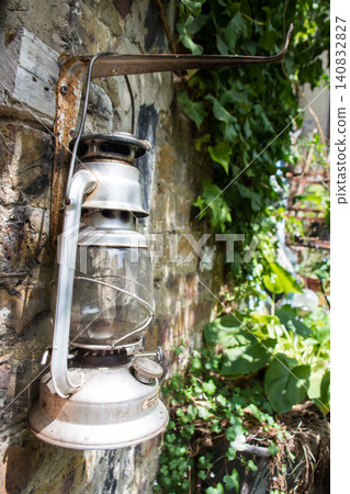 A retro lamp hanging on a wall surrounded by greenery, on Eel Pie Island, a suburb of London. A retro lamp hanging on a wall surrounded by greenery, on Eel Pie Island, a suburb of London. 140832827