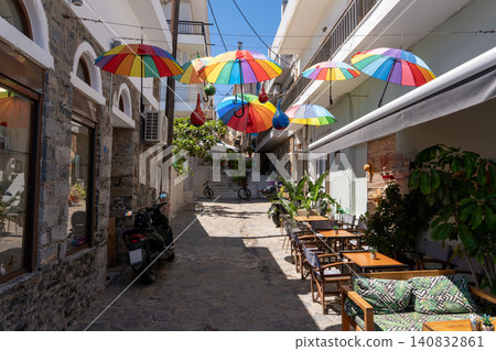 Colorful umbrellas hanging over a narrow street with outdoor cafe tables in Elounda, Crete, Greece Colorful umbrellas hanging over a narrow street with outdoor cafe tables in Elounda, Crete, Greece 140832861