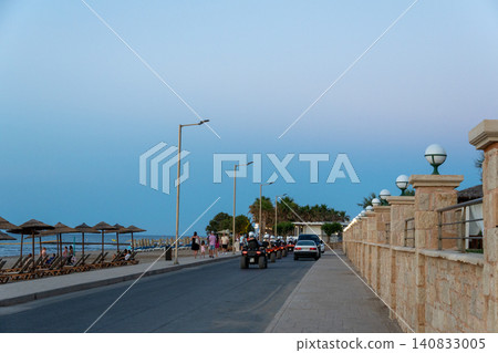 Tourists on quad bikes riding along coastal resort promenade at twilight Tourists on quad bikes riding along coastal resort promenade at twilight 140833005
