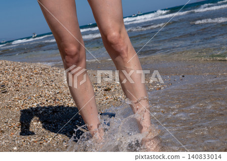 Refreshing sea wave splashing on woman legs at summer beach 140833014