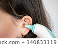 Girl with white digital thermometer near her ear. Digital infrared device for temperature measurement at home and in hospital. 140833119