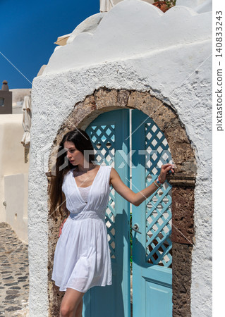 Beautiful young woman in white dress posing near blue wooden door in Santorini Greece Beautiful young woman in white dress posing near blue wooden door in Santorini Greece 140833243