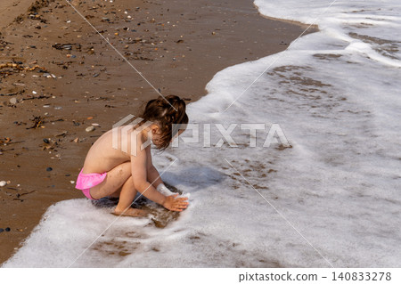 Little girl playing with sea foam on sand beach Little girl playing with sea foam on sand beach 140833278