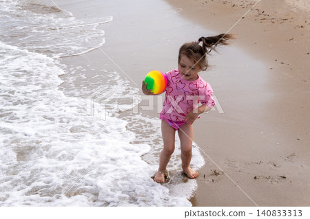 Little girl playing with colorful ball on sandy sea beach Little girl playing with colorful ball on sandy sea beach 140833313