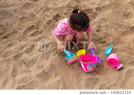 Little girl playing with plastic toys in sand on beach 140833314
