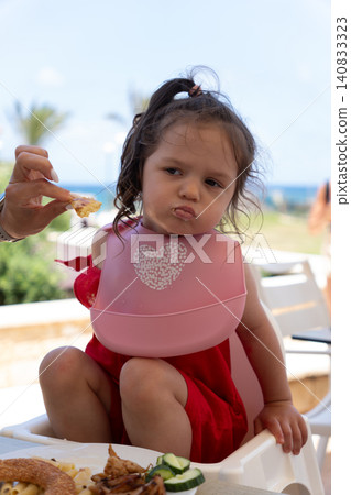 Vertical portrait of mother feeding grumpy little girl at restaurant Vertical portrait of mother feeding grumpy little girl at restaurant 140833323