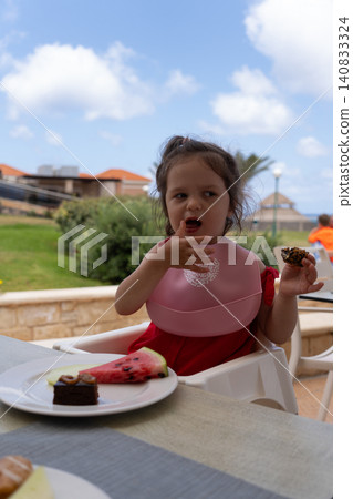 Vertical portrait of cute toddler girl eating dessert at outdoor restaurant Vertical portrait of cute toddler girl eating dessert at outdoor restaurant 140833324