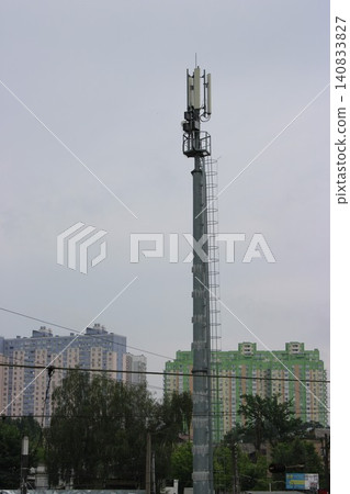 Cellular communication tower with antennas standing tall against a backdrop of residential apartment buildings under a cloudy sky in an urban setting Cellular communication tower with antennas standing tall against a backdrop of residential apartment buildings under a cloudy sky in an urban setting 140833827