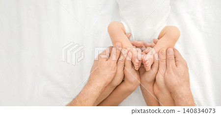 Close-up of a newborn baby's small legs in the arms of its parents and an older sister. Banner on the topic of care and parenting, and children's health Close-up of a newborn baby's small legs in the arms of its parents and an older sister. Banner on the topic of care and parenting, and children's health 140834073