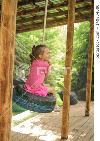A happy child is swinging on a wheel tire suspended from a rope. Children's activities during summer vacations A happy child is swinging on a wheel tire suspended from a rope. Children's activities during summer vacations 140834080