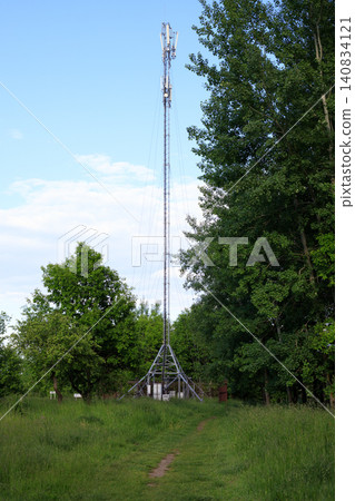 Tall cellular connection tower rises above green trees and field under a cloudy sky Tall cellular connection tower rises above green trees and field under a cloudy sky 140834121