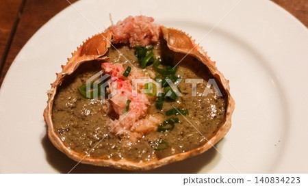 close up of grilled crab shell with kani miso, crab meat, and green onion garnish, which is a traditional Japanese seafood delicacy called Crab Miso on Shell on a white plate with copy space close up of grilled crab shell with kani miso, crab meat, and green onion garnish, which is a traditional Japanese seafood delicacy called Crab Miso on Shell on a white plate with copy space 140834223