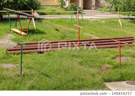 Long steel pipes lying on the lawn near apartment building playground during utility replacement project Long steel pipes lying on the lawn near apartment building playground during utility replacement project 140834257