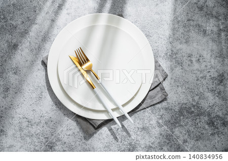 An empty white plates with a fork, knife and napkin on a gray concrete background An empty white plates with a fork, knife and napkin on a gray concrete background 140834956