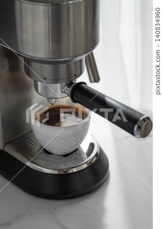 Espresso is brewed into a white cup in a modern coffee machine in soft morning light. Espresso is brewed into a white cup in a modern coffee machine in soft morning light. 140834960