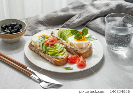 Two avocado toasts with egg, cream cheese, tomatoes, and basil on a concrete background Two avocado toasts with egg, cream cheese, tomatoes, and basil on a concrete background 140834966